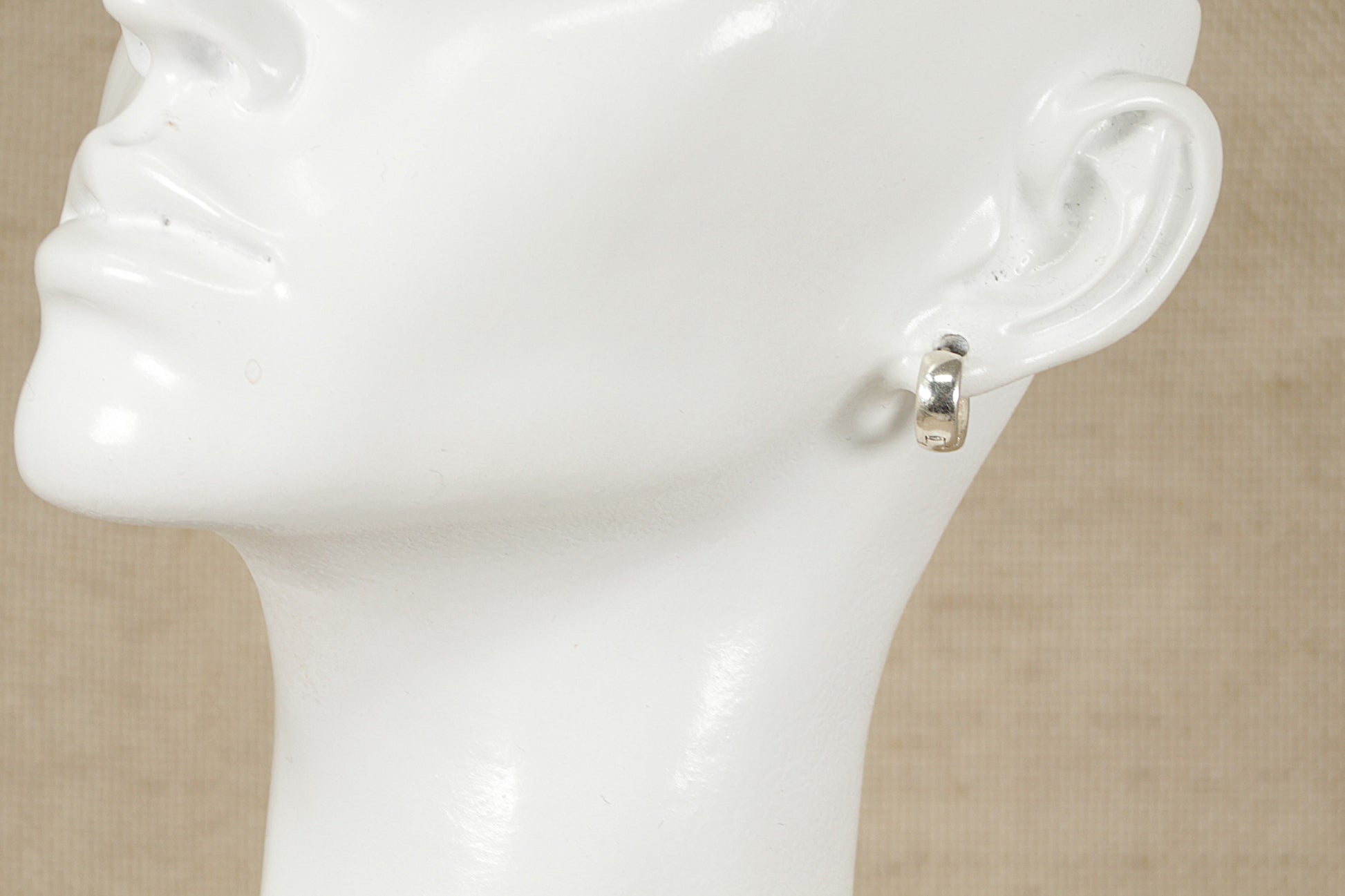 A pair of silver hoop earrings displayed on a mannequin head.