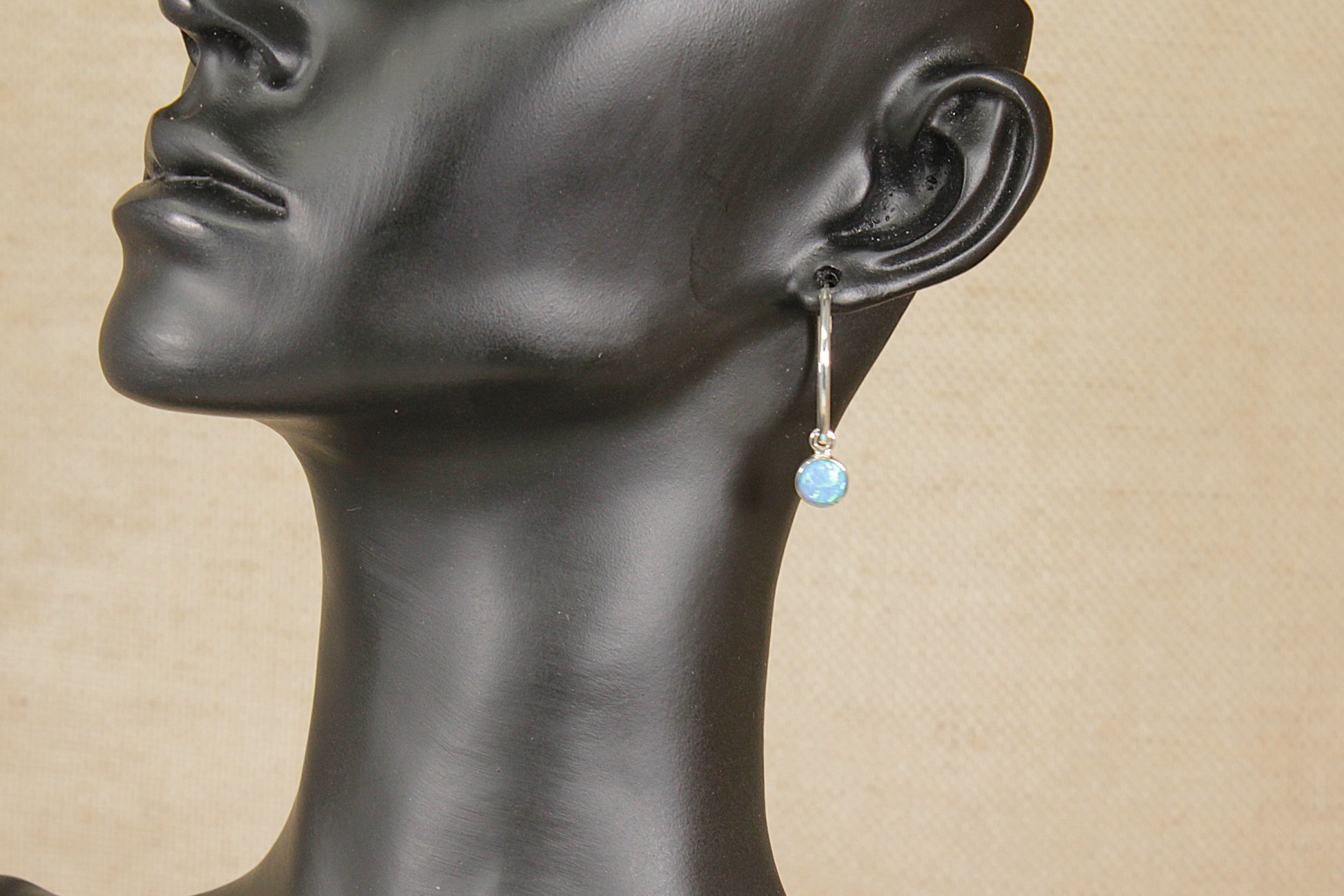 Mannequin head with a hoop earring featuring a blue opal gemstone on a beige background