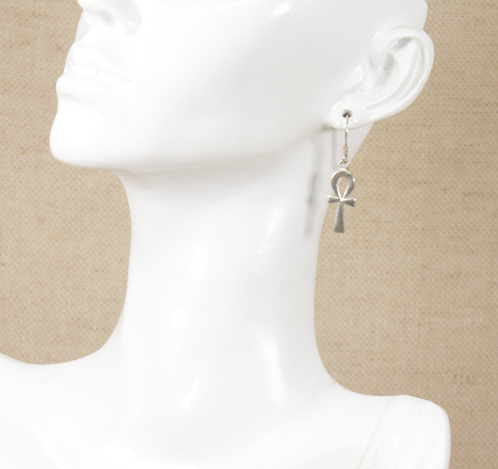 A pair of silver drop earrings with a key of life cross displayed on a mannequin head.
