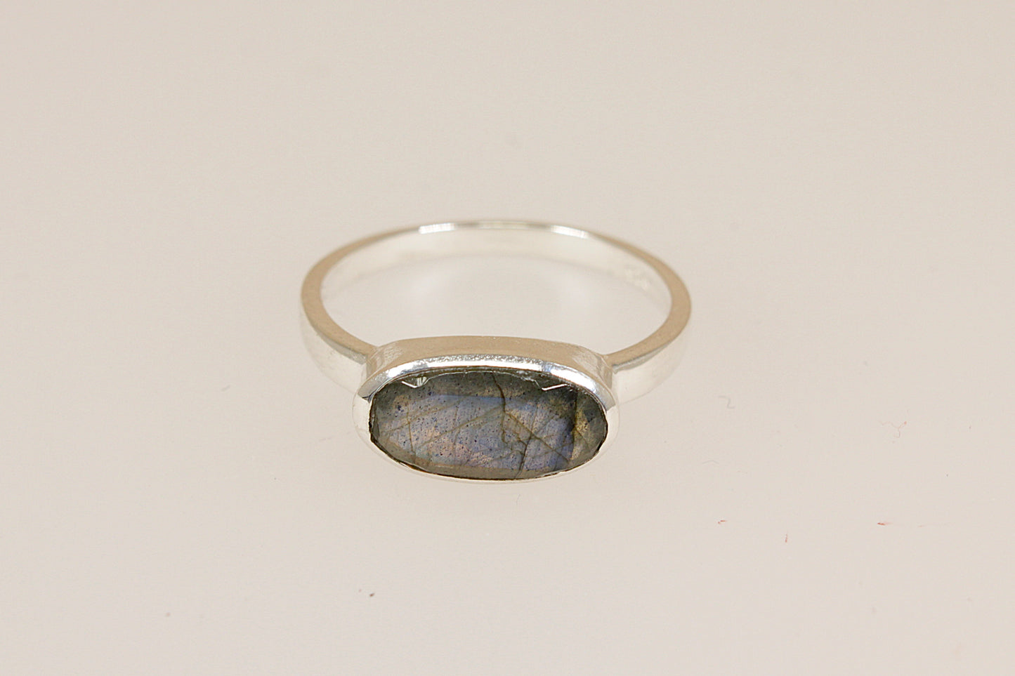 Silver ring with a labradorite stone on a beige background