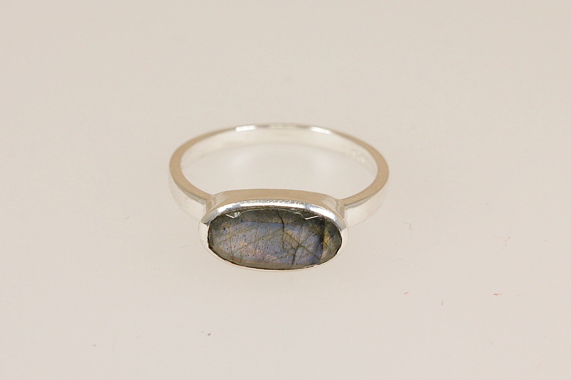 Silver ring with a labradorite stone on a beige background