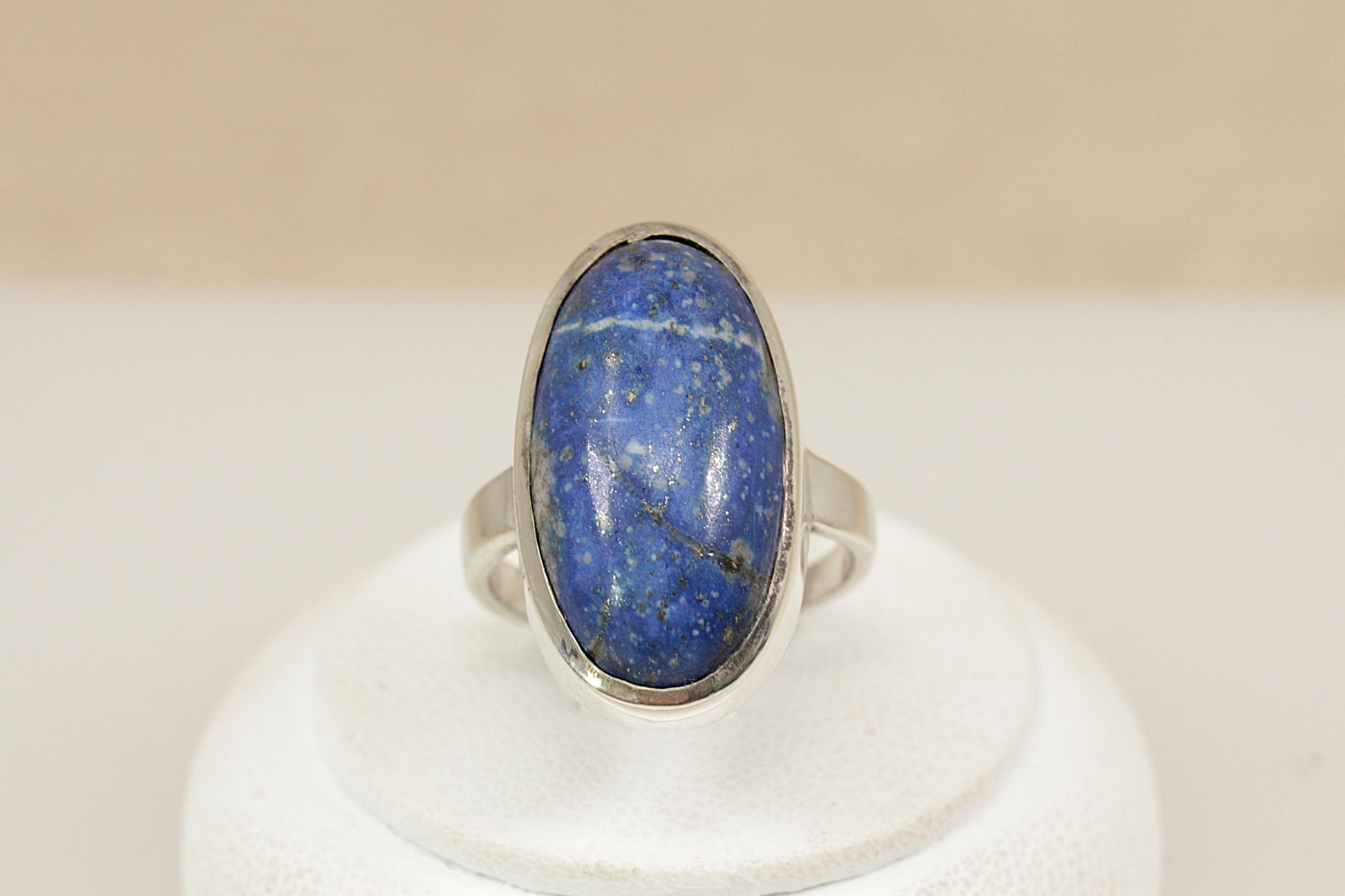 A striking Sterling Silver statement ring, showcasing a rich oval cabochon Lapis Lazuli gemstone, bezel set for a smooth and secure finish. The deep blue stone is beautifully accented with natural silver pyrite flecks, giving it a starry, celestial appearance that makes it truly captivating.
The setting is bold yet refined, allowing the natural beauty of the stone to take centre stage. The ring features continental silver hallmarks on the outside of the band, UK finger size N.