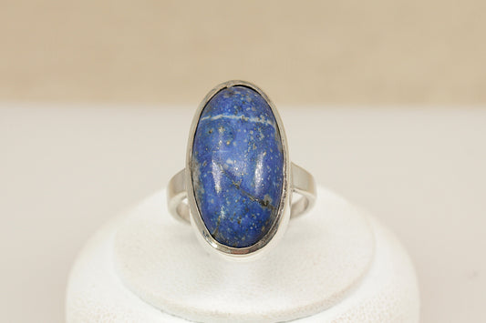 A striking Sterling Silver statement ring, showcasing a rich oval cabochon Lapis Lazuli gemstone, bezel set for a smooth and secure finish. The deep blue stone is beautifully accented with natural silver pyrite flecks, giving it a starry, celestial appearance that makes it truly captivating.
The setting is bold yet refined, allowing the natural beauty of the stone to take centre stage. The ring features continental silver hallmarks on the outside of the band, UK finger size N.
