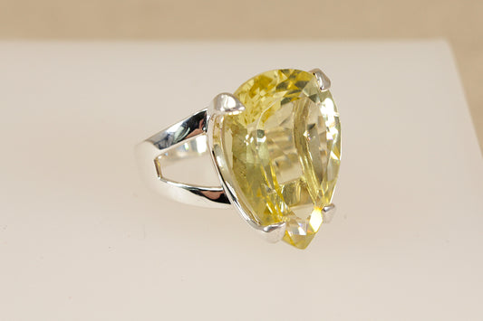Silver ring with a pear-shaped yellow lemon citrine gemstone on a beige background