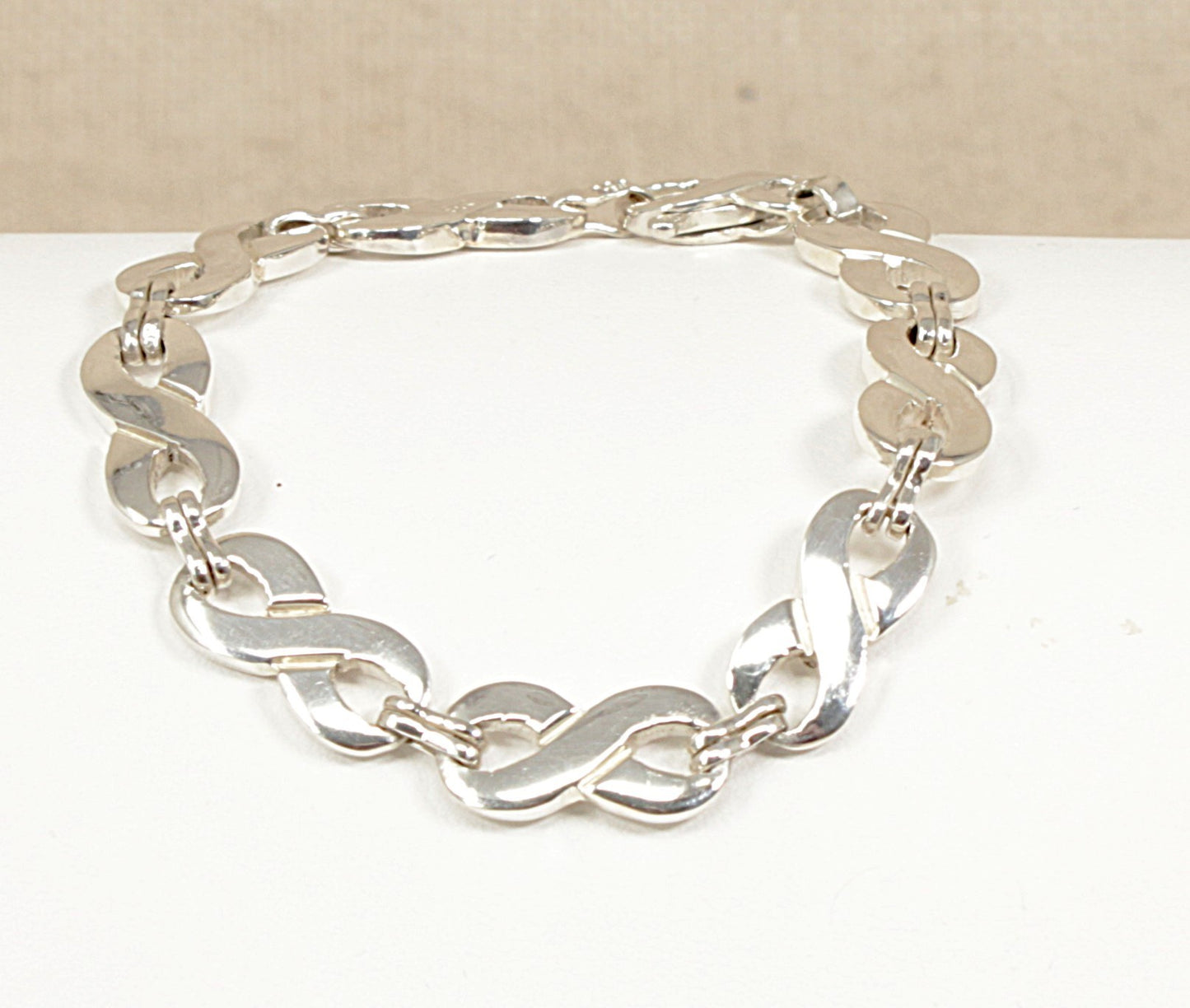 Sterling Silver bracelet with figure of eight links on a white surface with a beige background.
