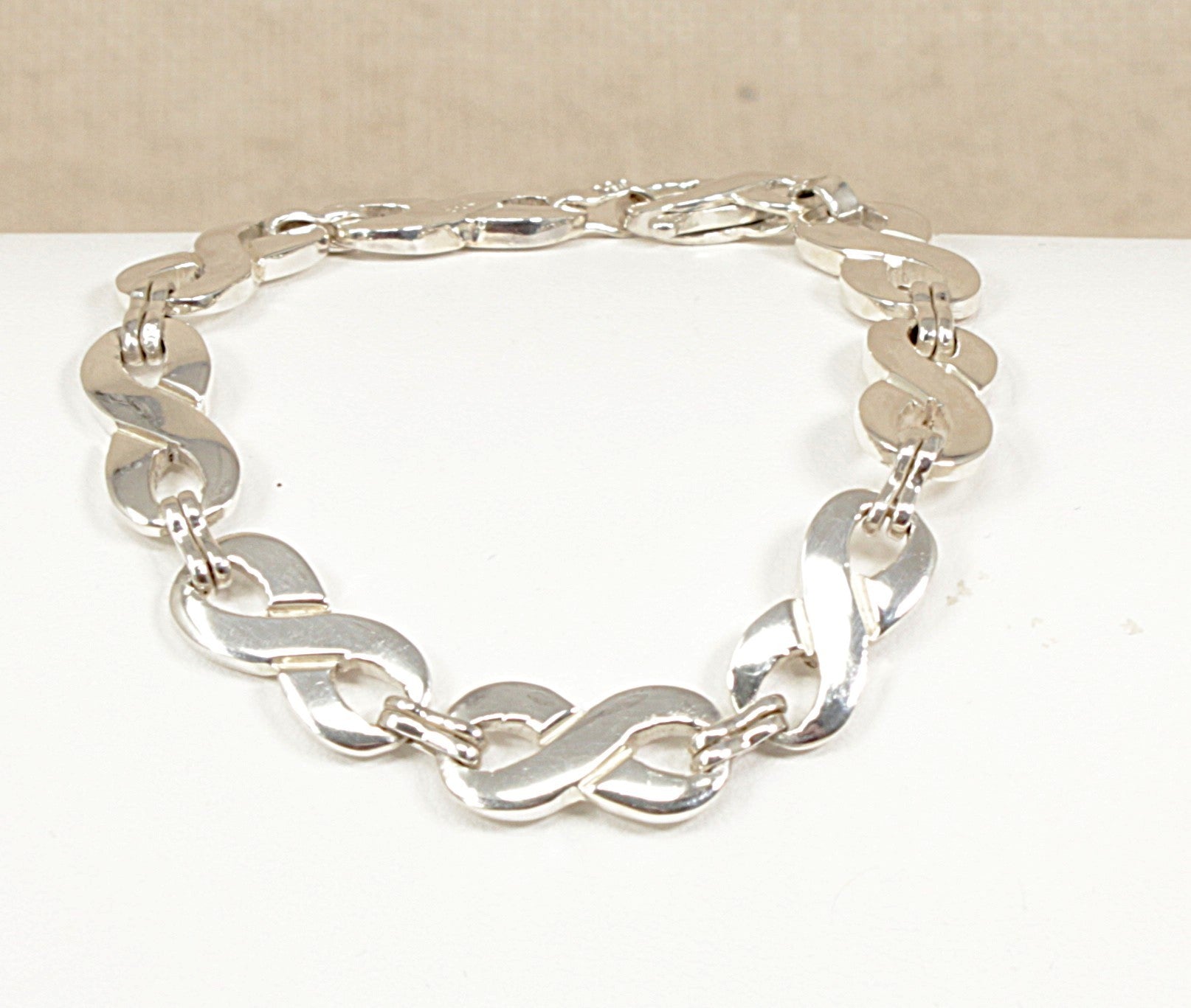 Sterling Silver bracelet with figure of eight links on a white surface with a beige background.
