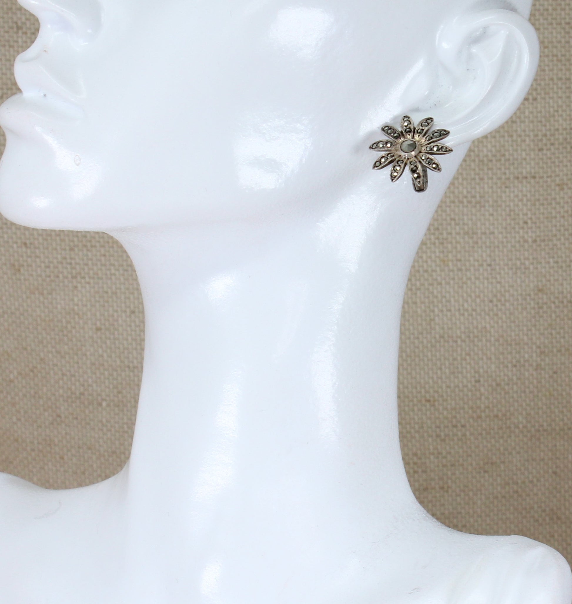 A pair of silver clip-on earrings with marcasite encrusted in a floral pattern displayed on a mannequin head.