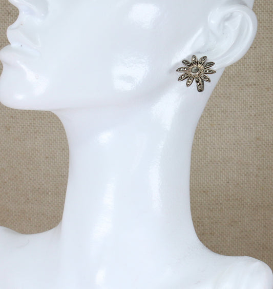 A pair of silver clip-on earrings with marcasite encrusted in a floral pattern displayed on a mannequin head.