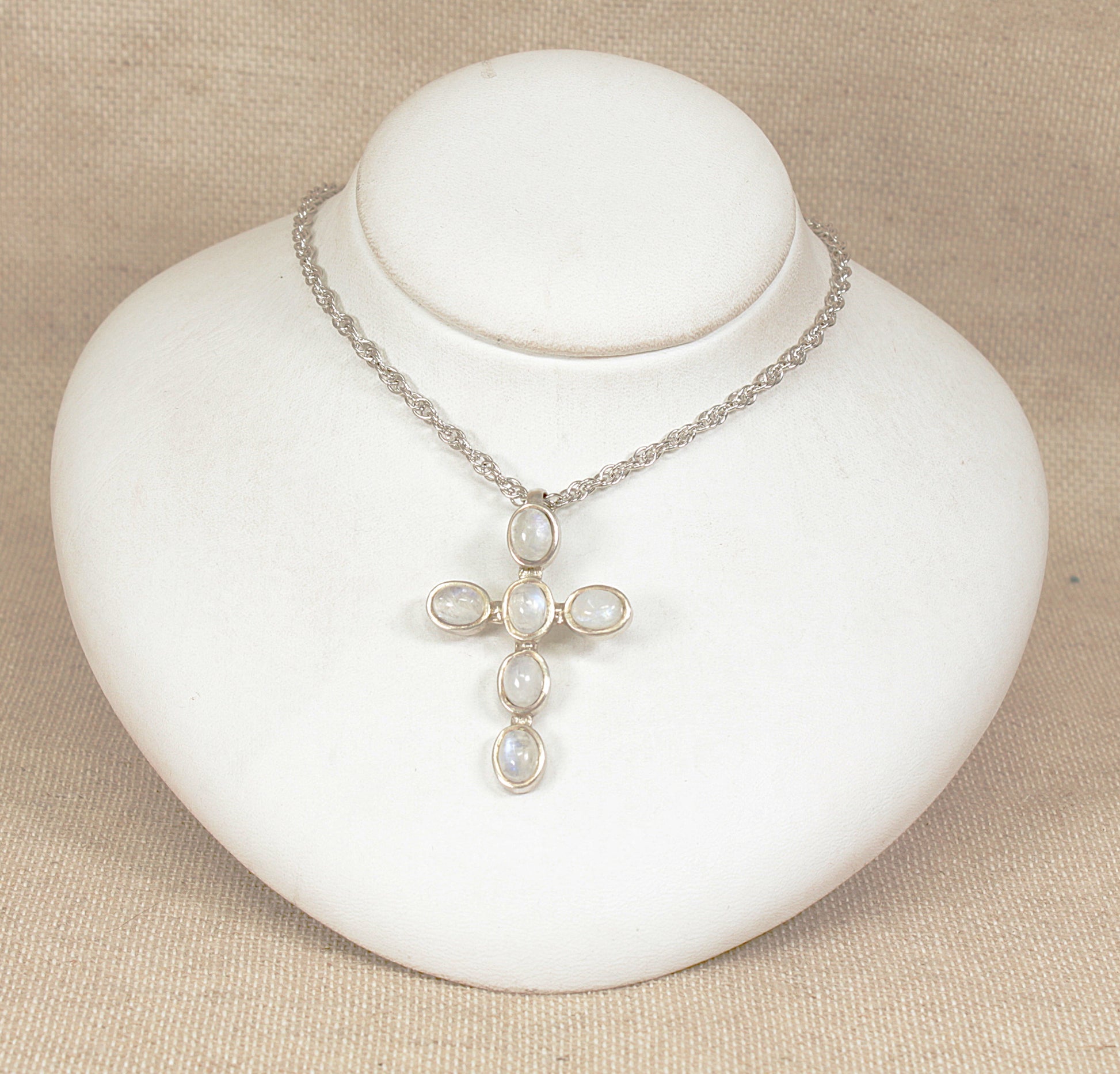 Silver cross necklace with moonstone  on a white mannequin bust against a beige background
