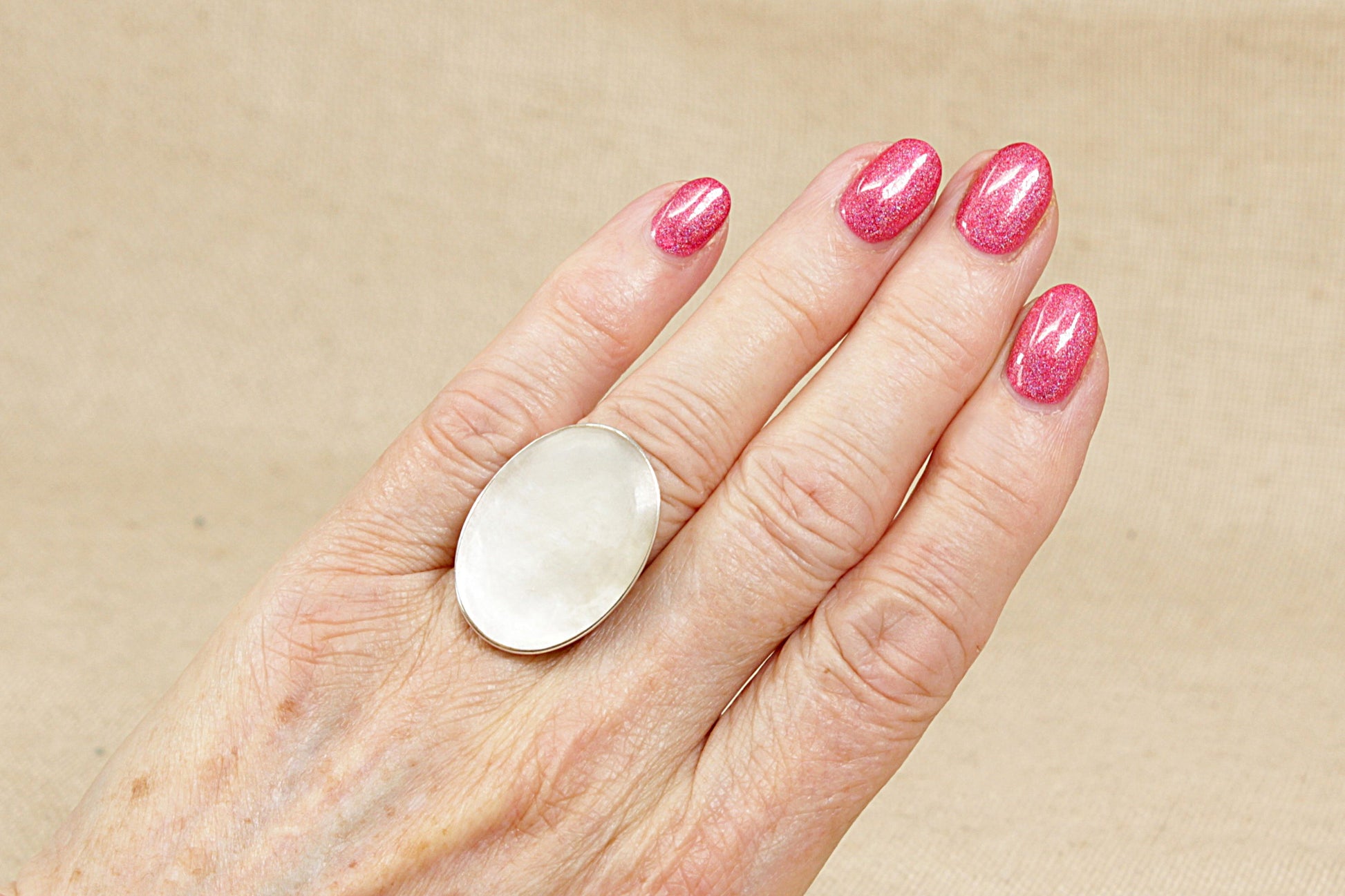 A bold and elegant sterling silver statement ring, featuring a luminous oval Mother of Pearl centrepiece. The stone is bezel set in a smooth, flat-topped setting, allowing its soft, iridescent shimmer to take centre stage. Measuring 3cm in length, the ring makes a striking impression while remaining effortlessly wearable. UK finger size O.