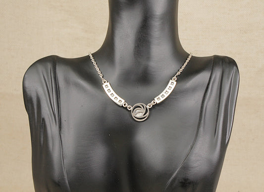 A distinctive and elegant solid Sterling Silver necklet, inspired by the iconic designs of renowned Scottish artist Charles Rennie Mackintosh. This beautifully crafted piece features a central round pendant adorned with a nature-inspired petal motif, capturing the essence of Mackintosh’s celebrated blend of organic and geometric forms. Length: Adjustable from 16 to 17 inches.