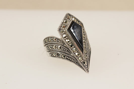 A dramatic and beautifully crafted Art Deco-inspired sterling silver ring, featuring a striking geometric pear-shaped onyx at its centre. The onyx is set within a matching pear-shaped bezel, fully encrusted with glittering marcasite stones that accentuate its bold silhouette. UK finger size M.