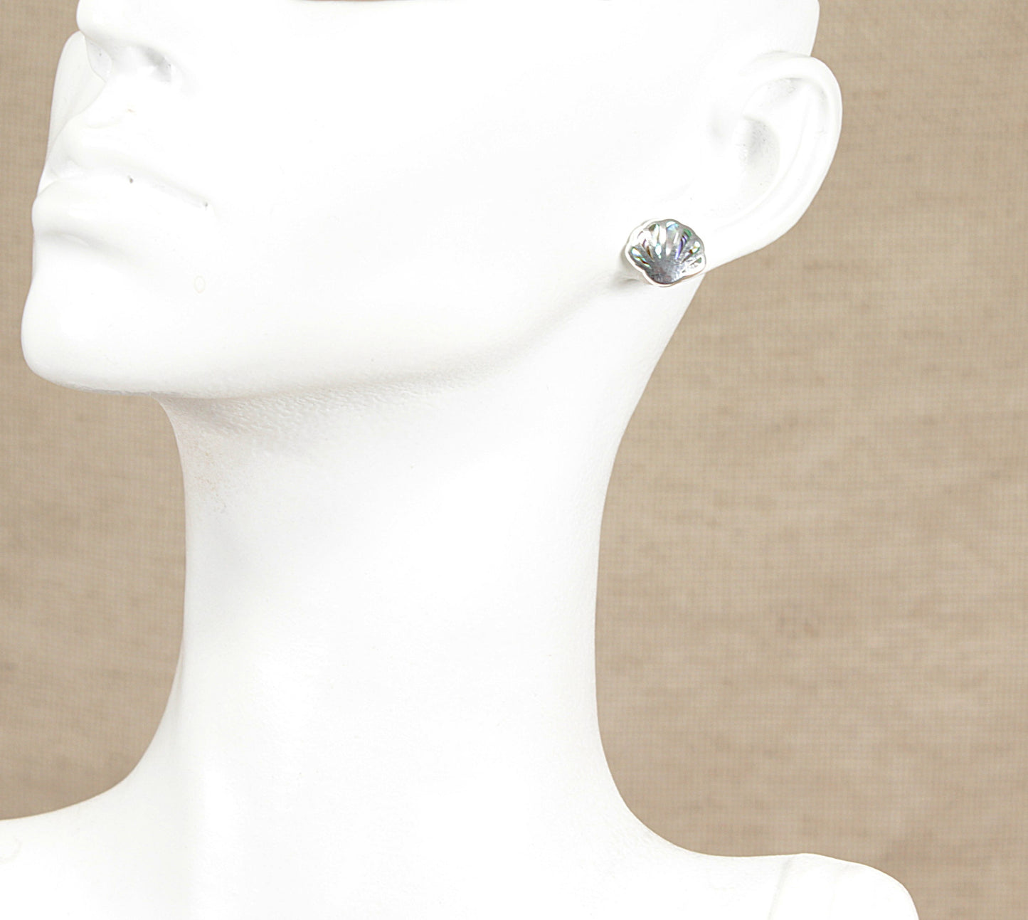 Silver paua stud earring on a mannequin ear against a beige background