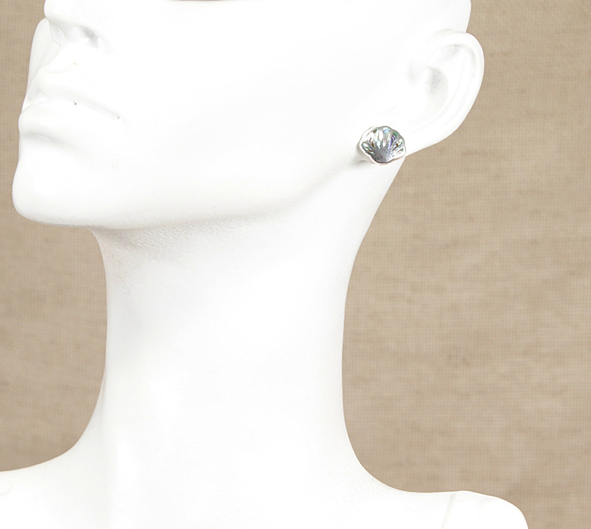 Silver paua stud earring on a mannequin ear against a beige background