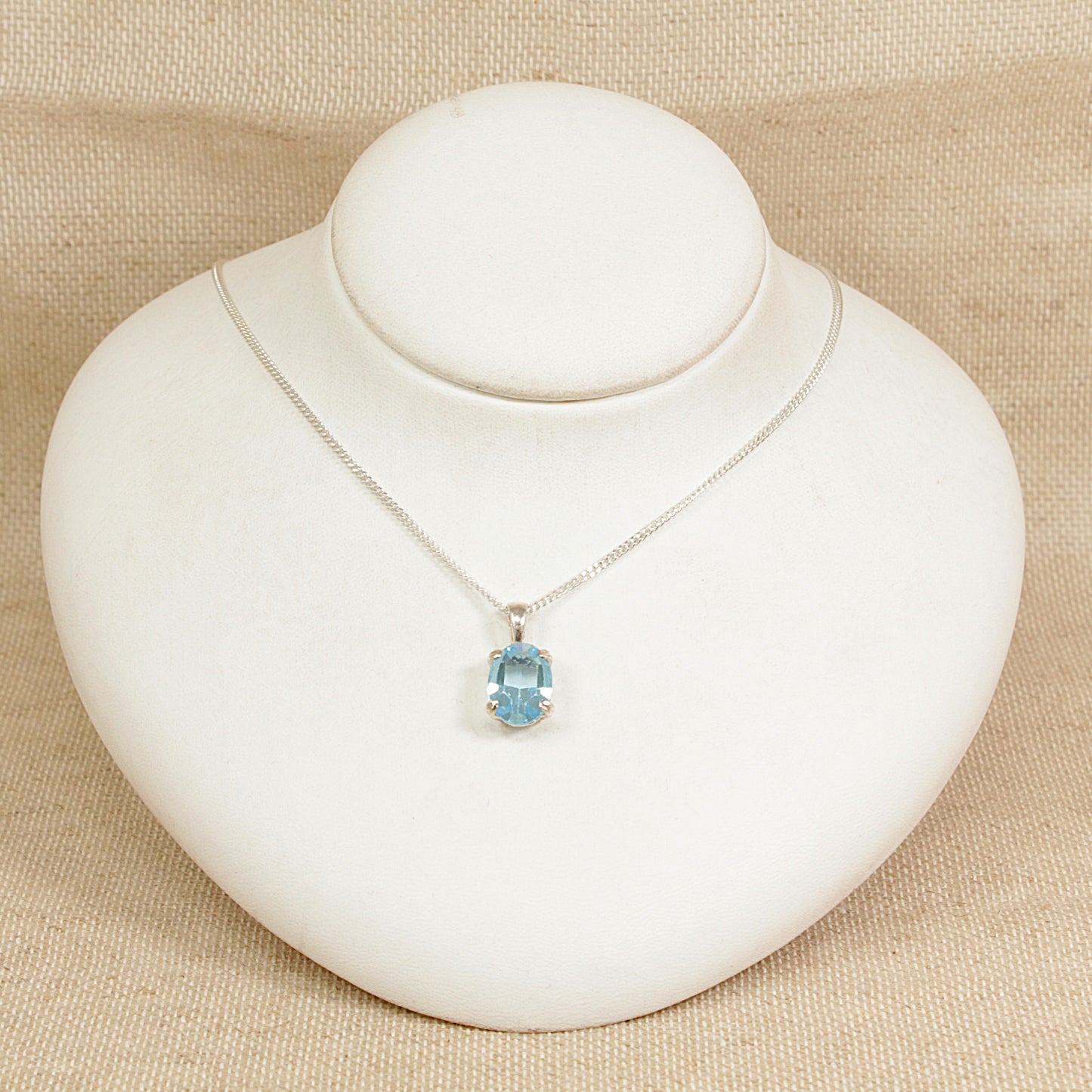 Necklace with a blue crystal pendant on a white mannequin bust against a beige background