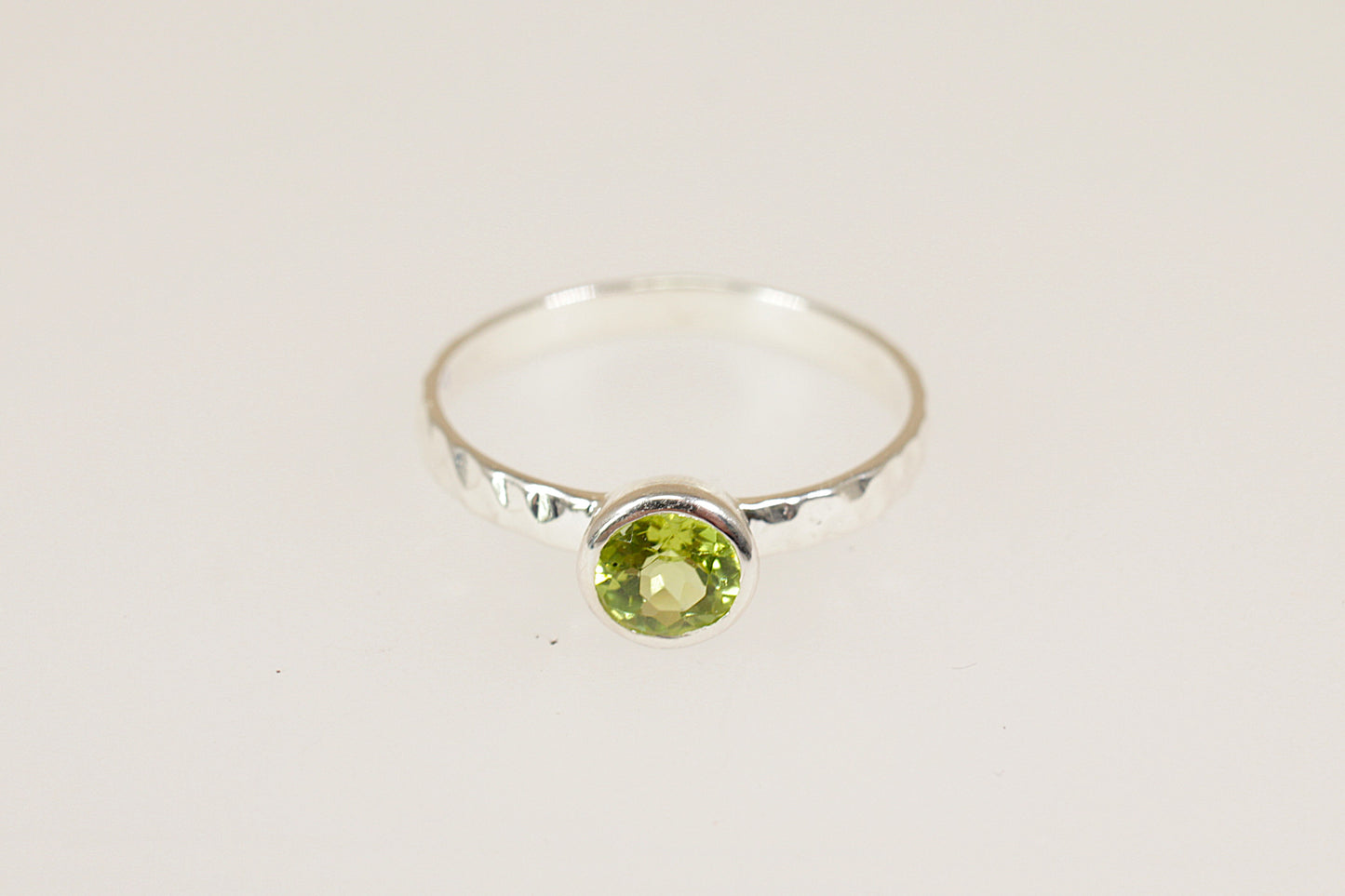 Silver ring with a green peridot gemstone on a light gray background