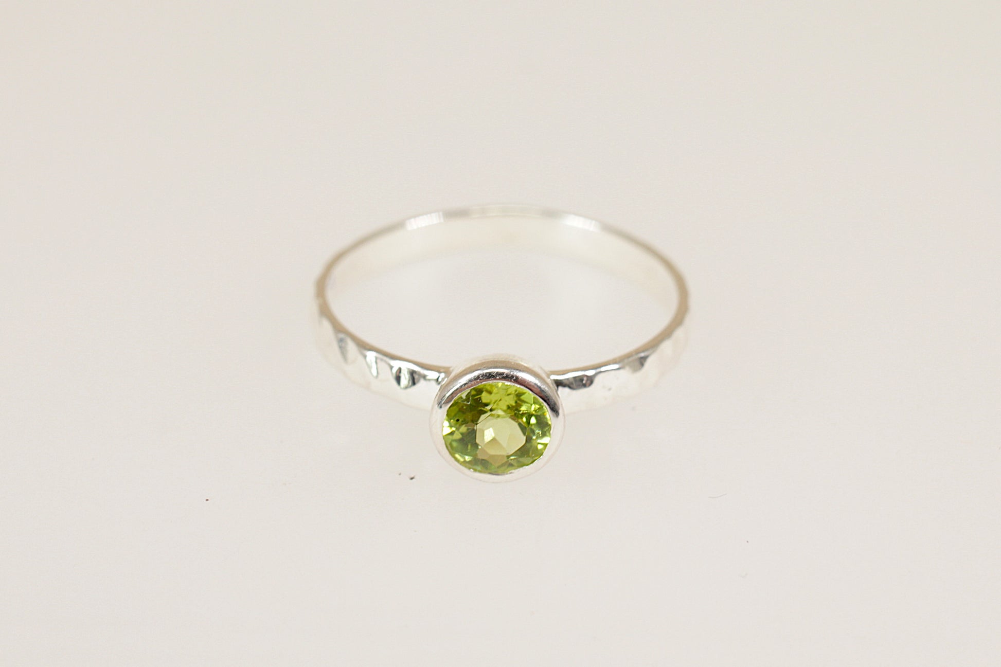 Silver ring with a green peridot gemstone on a light gray background