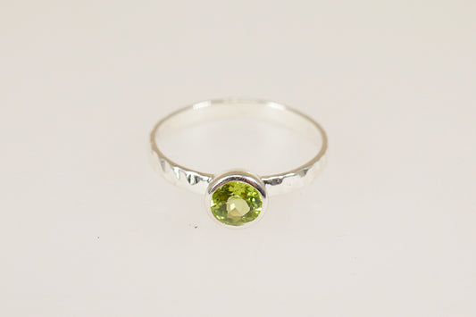 Silver ring with a green peridot gemstone on a light gray background