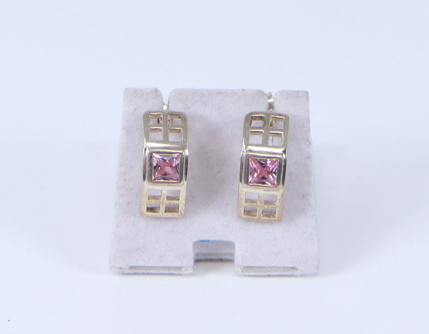 A pair of silver earrings with a geometric design and a center pink square crystal, displayed against a white background.