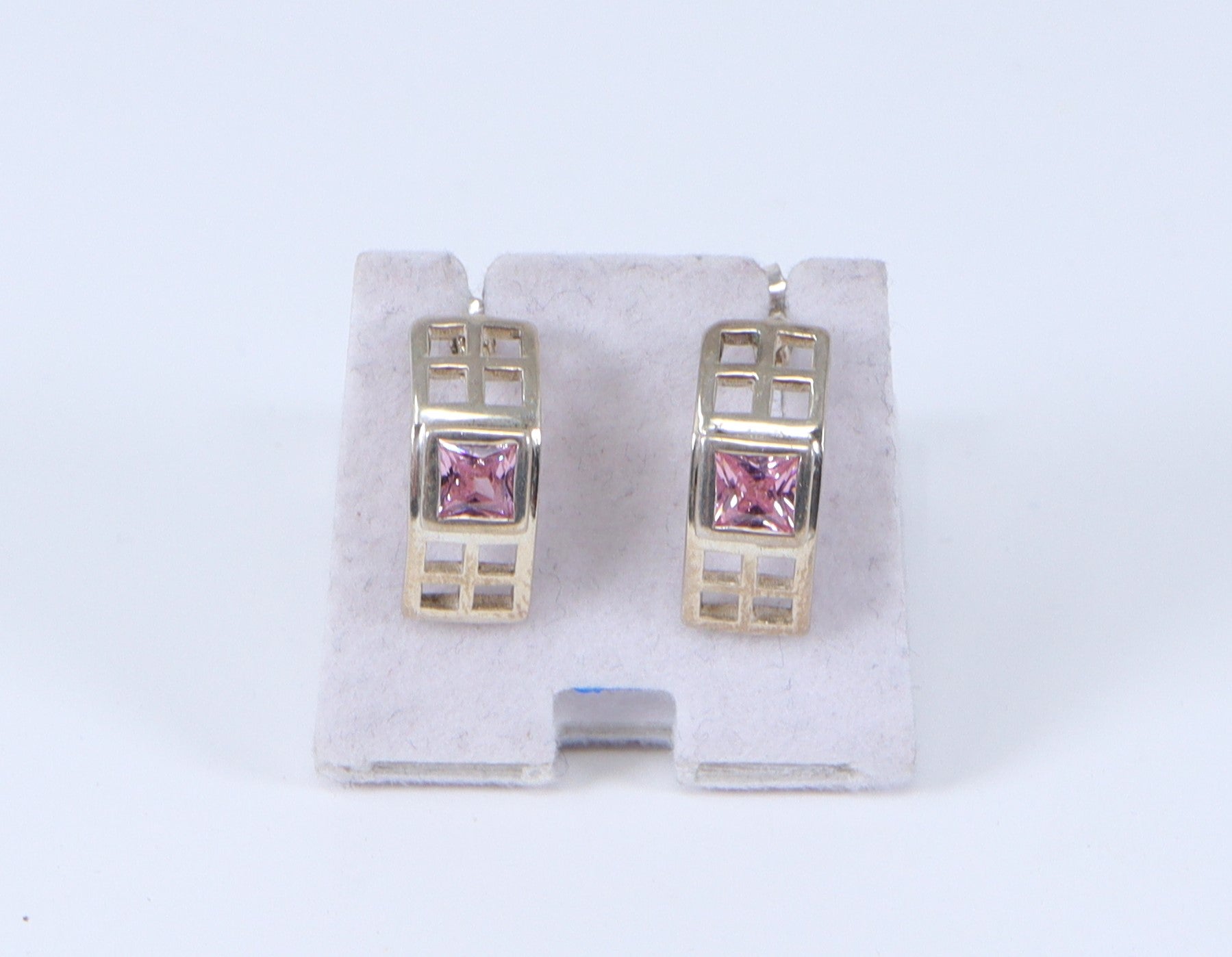 A pair of silver earrings with a geometric design and a center pink square crystal, displayed against a white background.