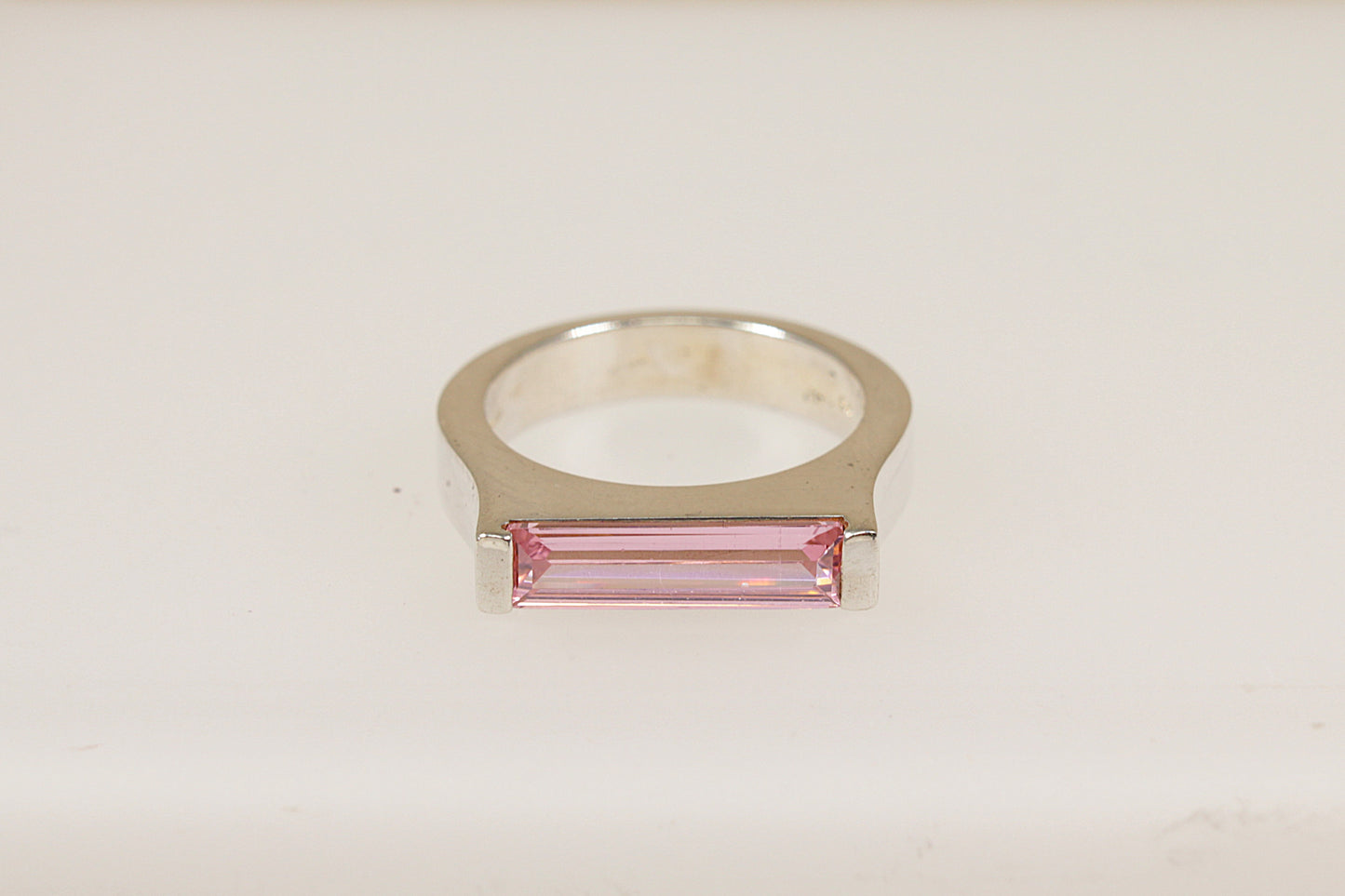 A silver ring with a horizontal pink crystal centerpiece, set on a white background.
