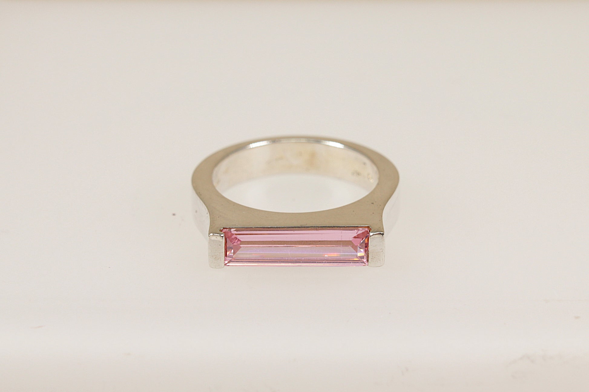A silver ring with a horizontal pink crystal centerpiece, set on a white background.