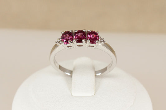 Silver ring with three pink tourmaline  gemstones on a white stand against a beige background