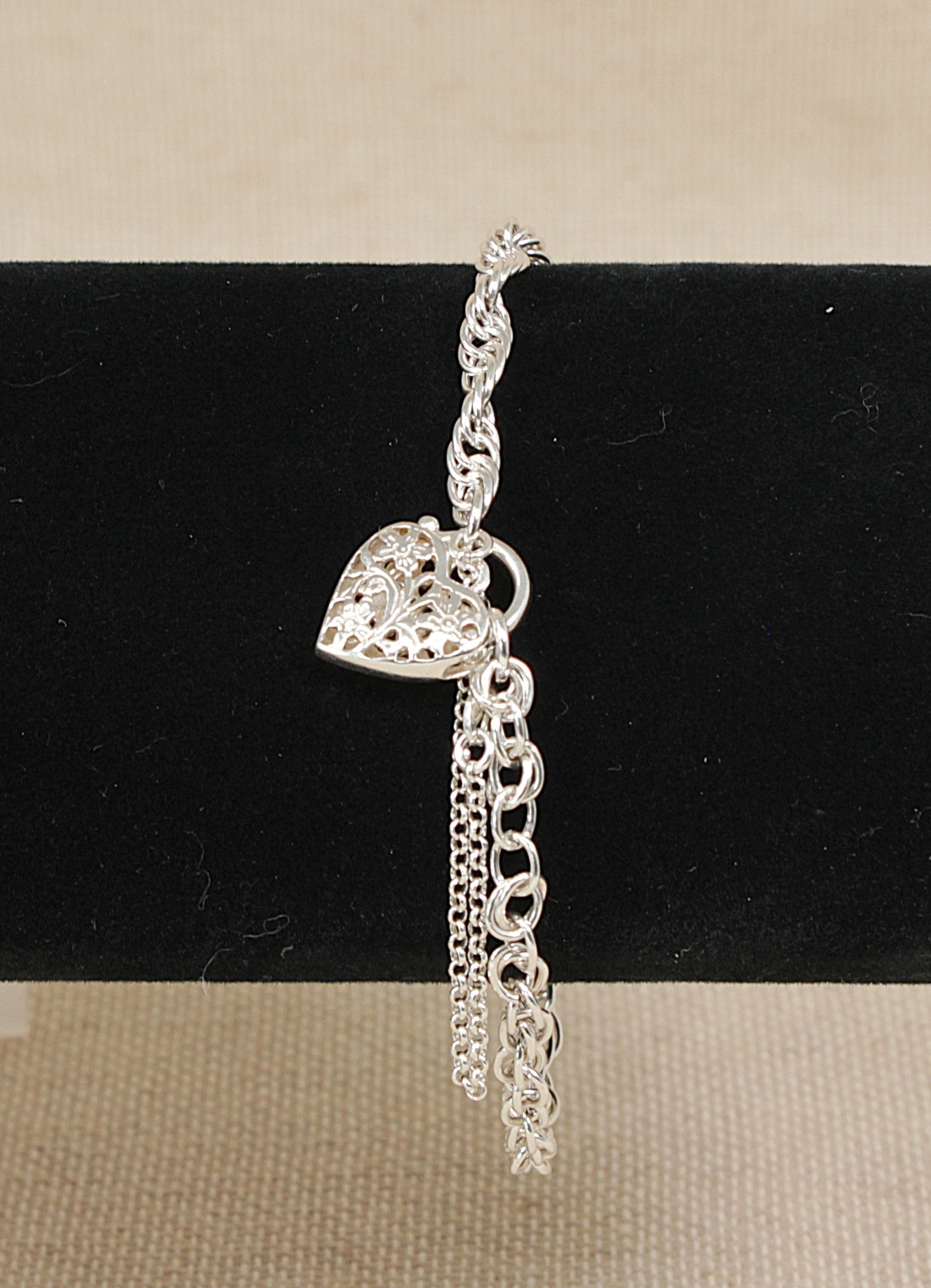 Silver bracelet with heart charm on a black stand