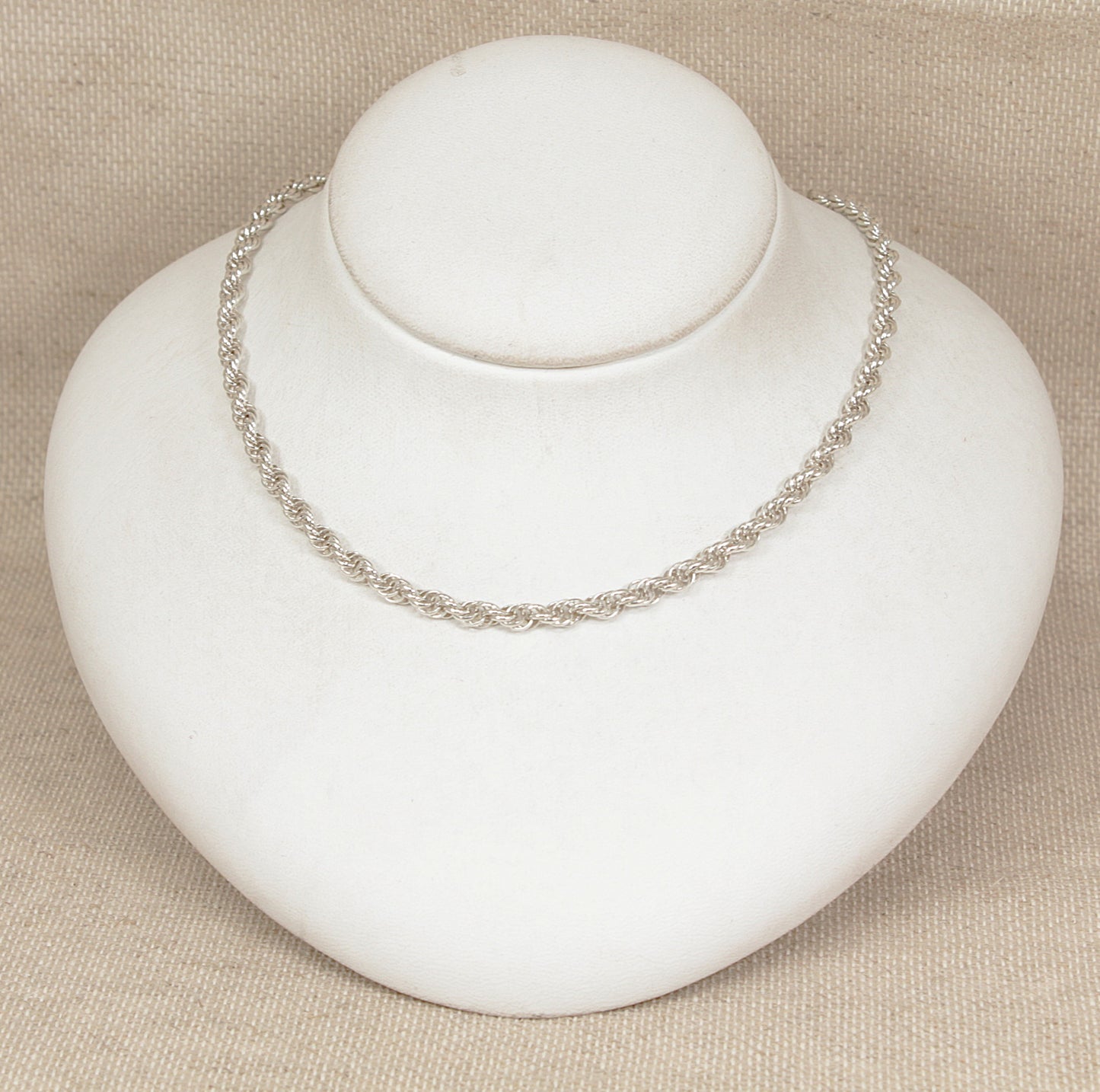Silver necklace on a white mannequin bust against a beige background