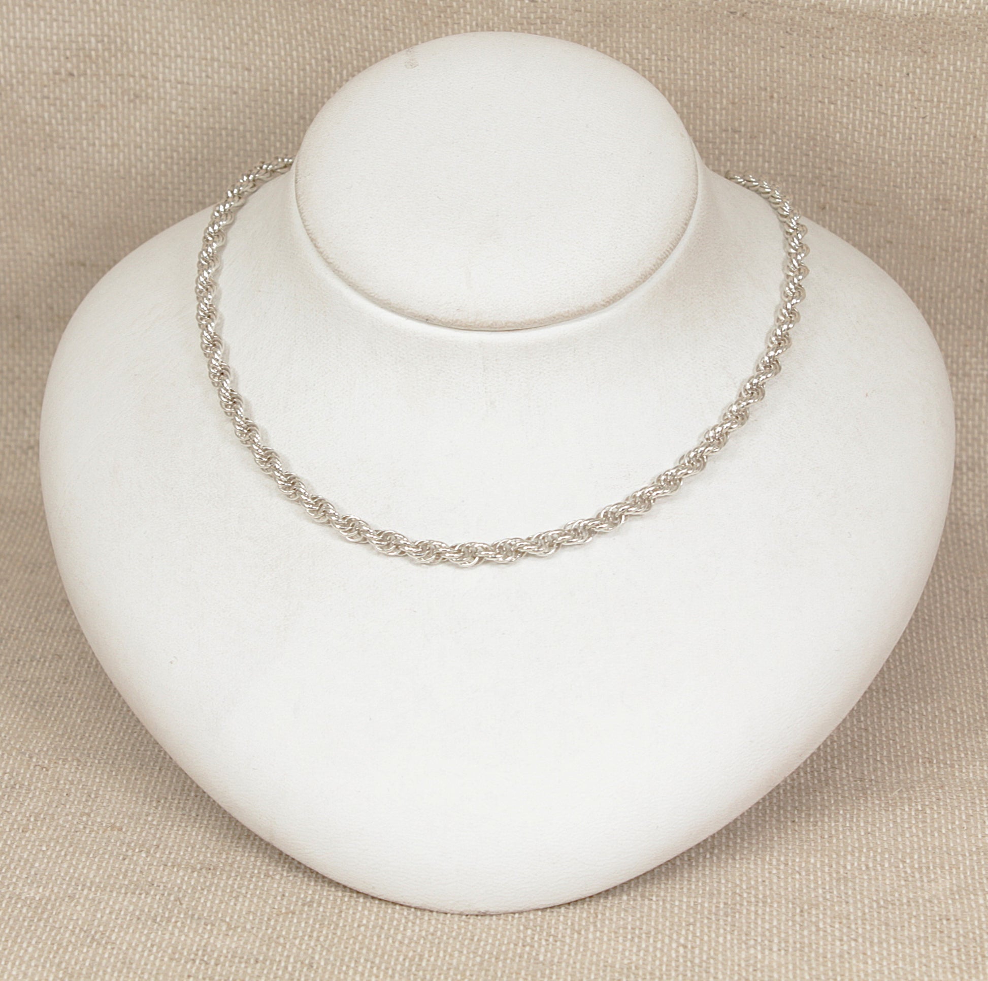 Silver necklace on a white mannequin bust against a beige background
