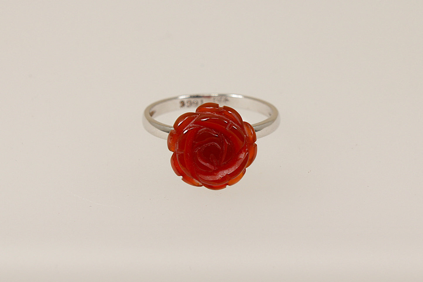 A silver ring with a carved red stone in the shape of a rose as the central element on a white background.