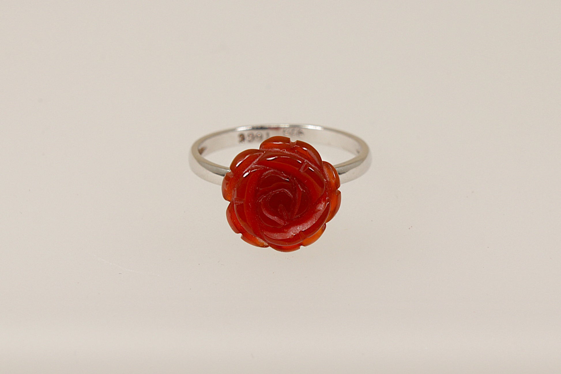 A silver ring with a carved red stone in the shape of a rose as the central element on a white background.