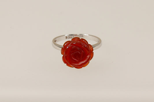 A silver ring with a carved red stone in the shape of a rose as the central element on a white background.
