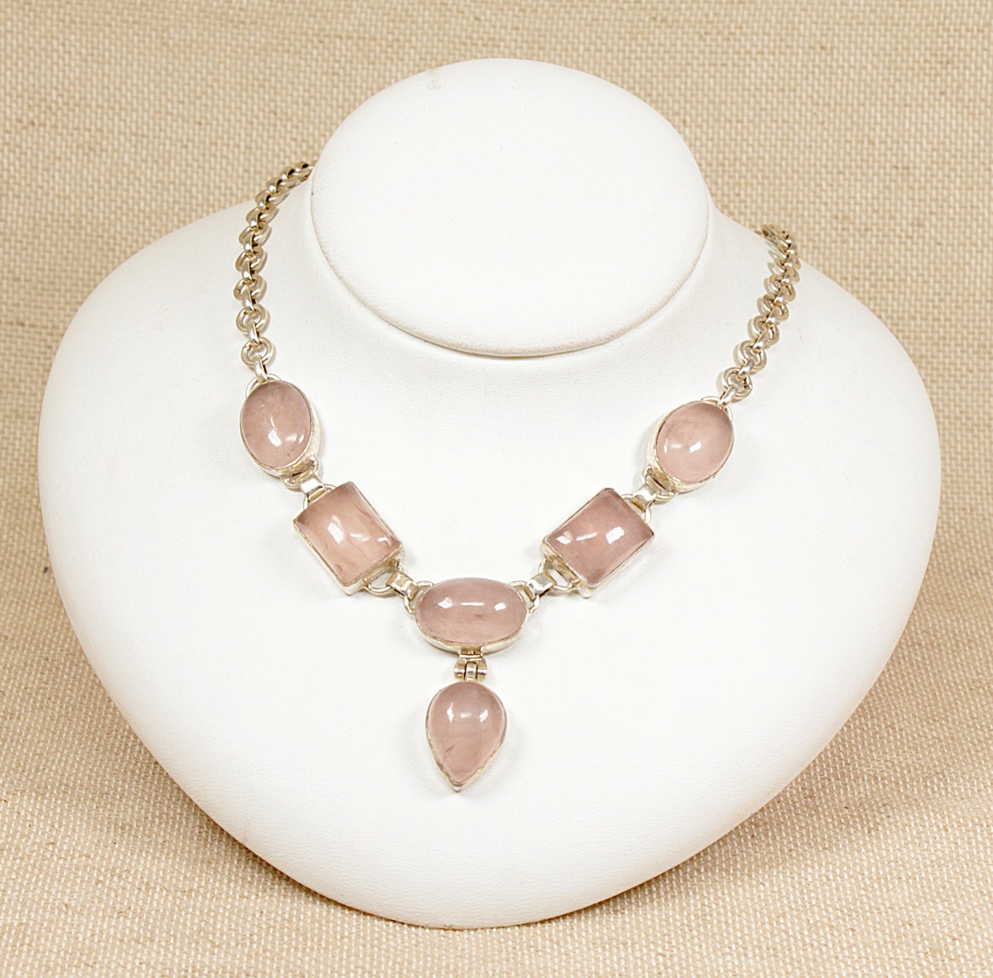 A silver necklace with rose quartz stones, featuring various cuts including ovals, rectangles, and teardrop, displayed on a white mannequin.