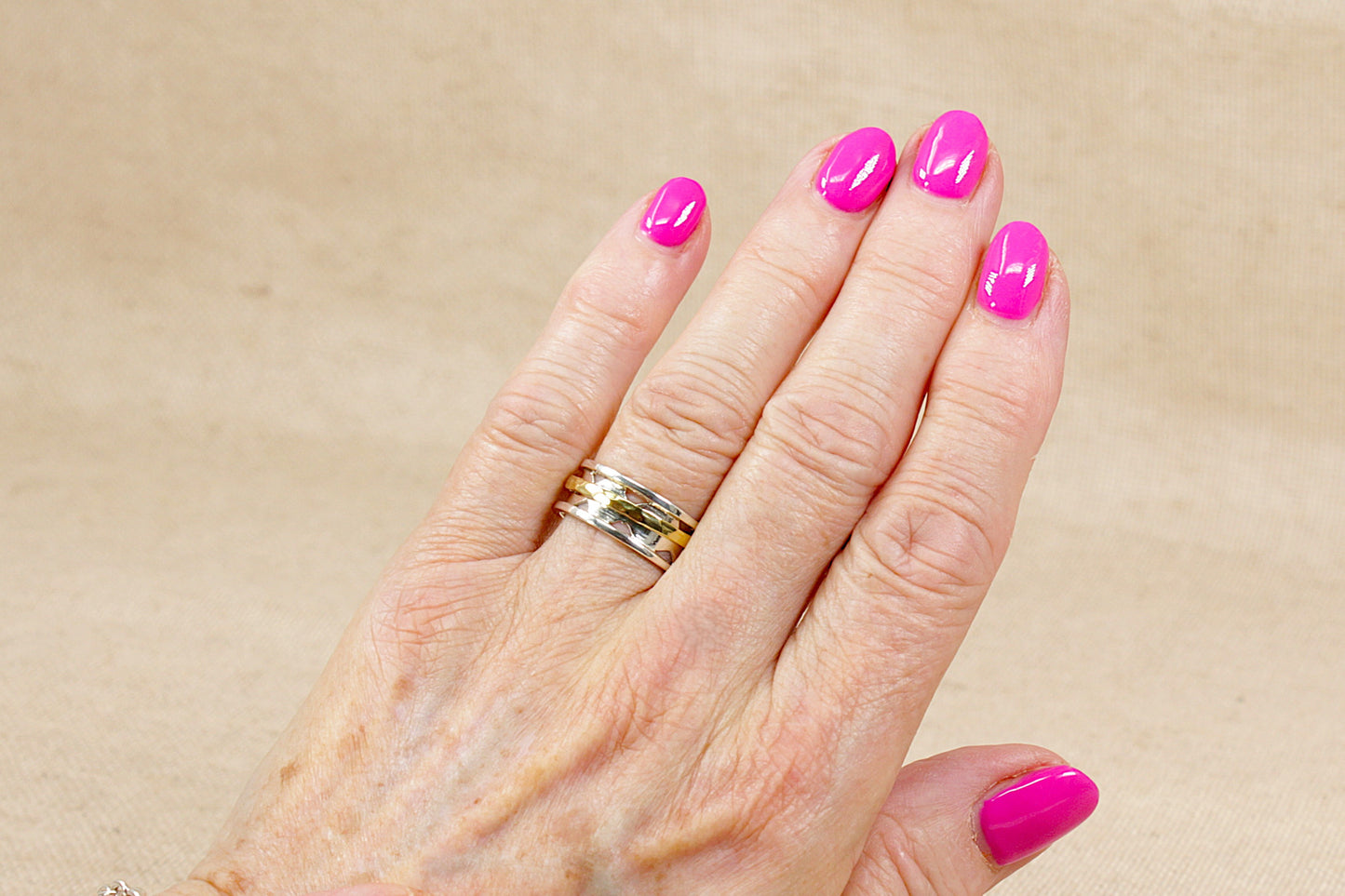 Hand with pink nail polish and silver spinner fidget rings on a beige background