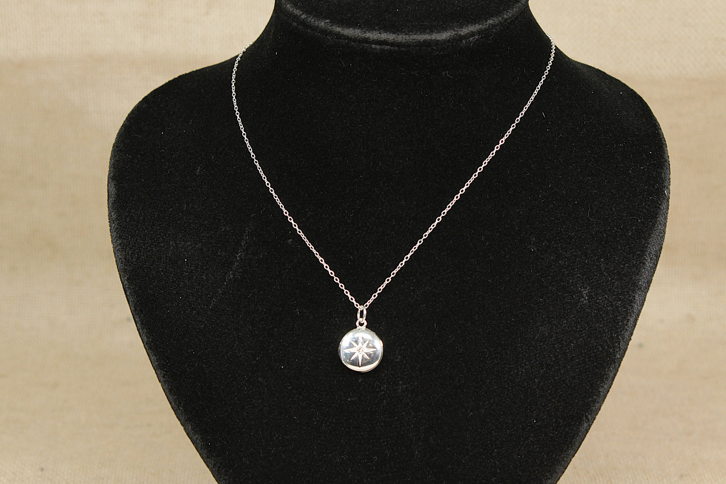 A silver locket with a central clear crystal on a black mannequin with a beige background