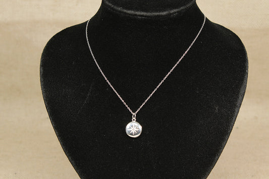 A silver locket with a central clear crystal on a black mannequin with a beige background