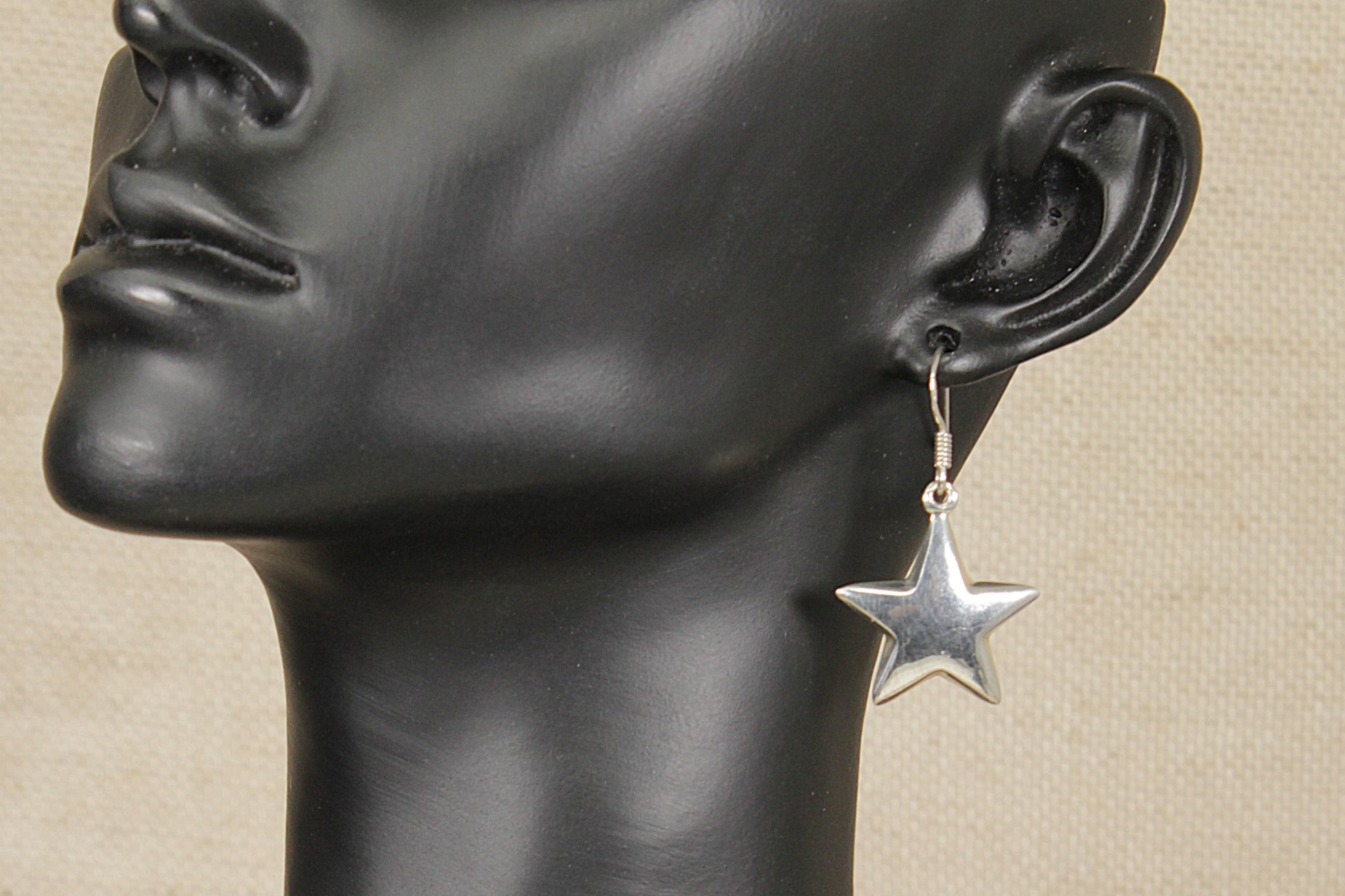 Star-shaped earring on a black mannequin head against a beige background