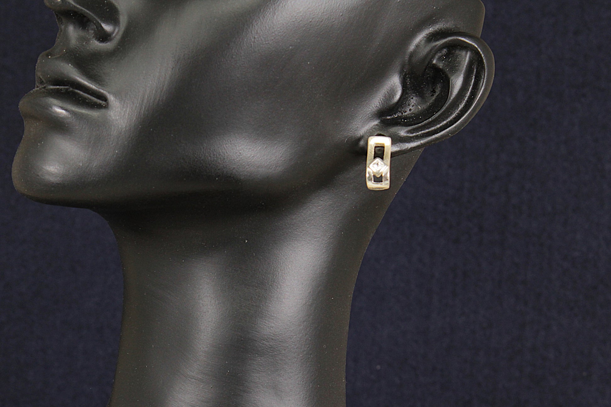Silver and crystal earring on a black mannequin ear against a dark background