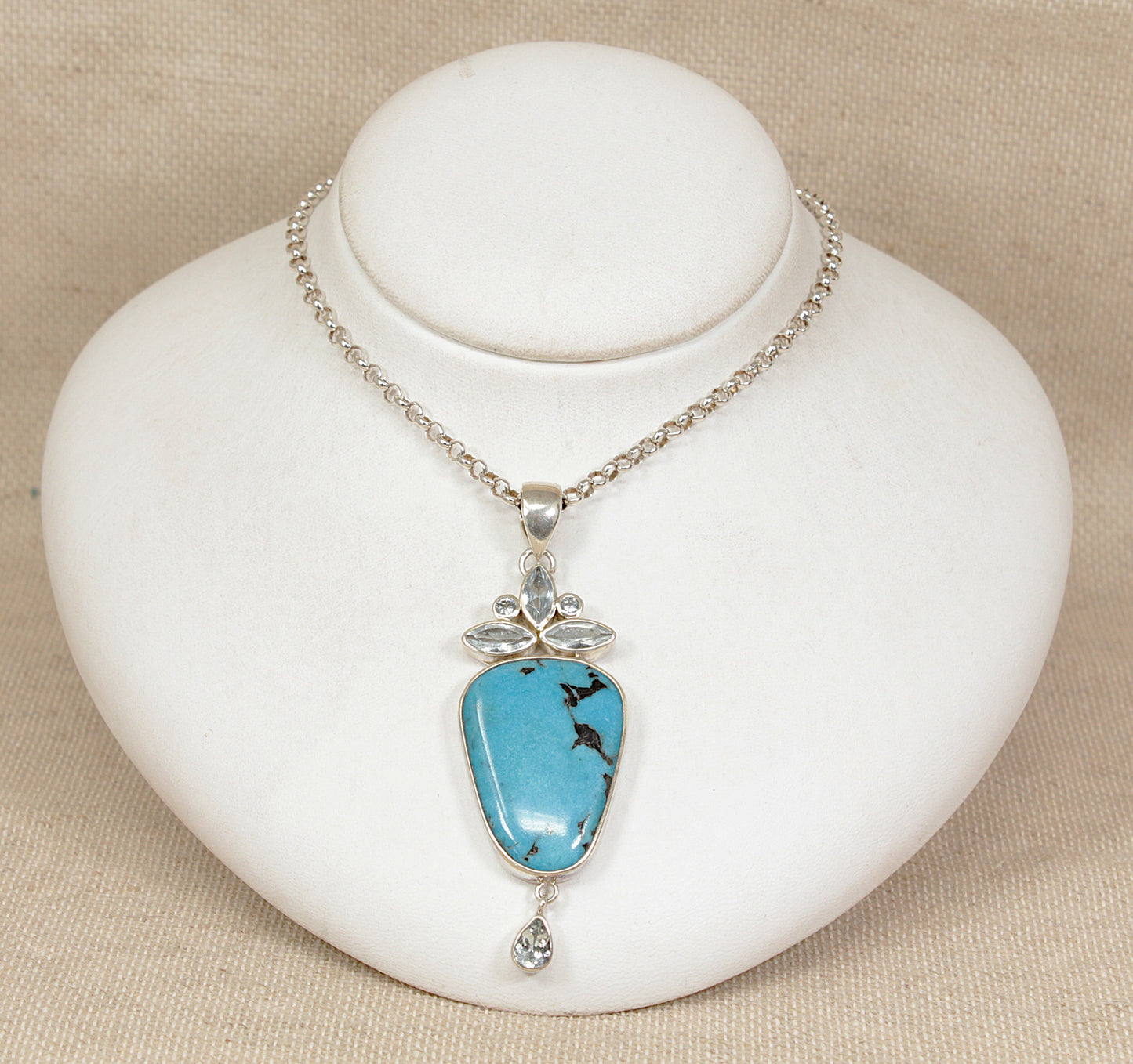 Turquoise silver pendant necklace on a white stand with beige background