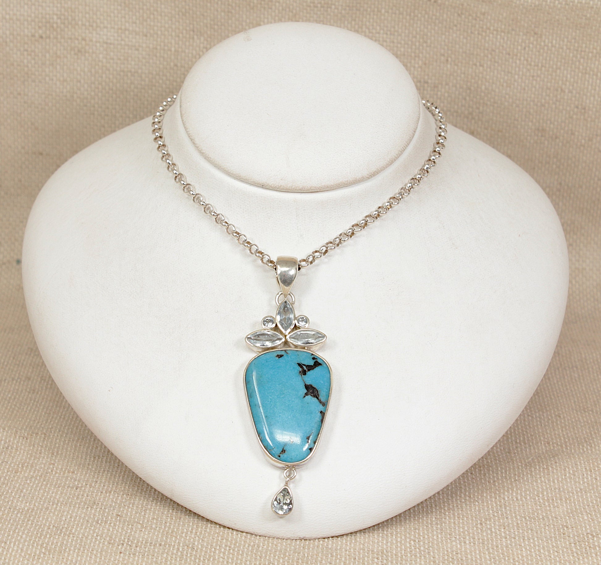 Turquoise silver pendant necklace on a white stand with beige background