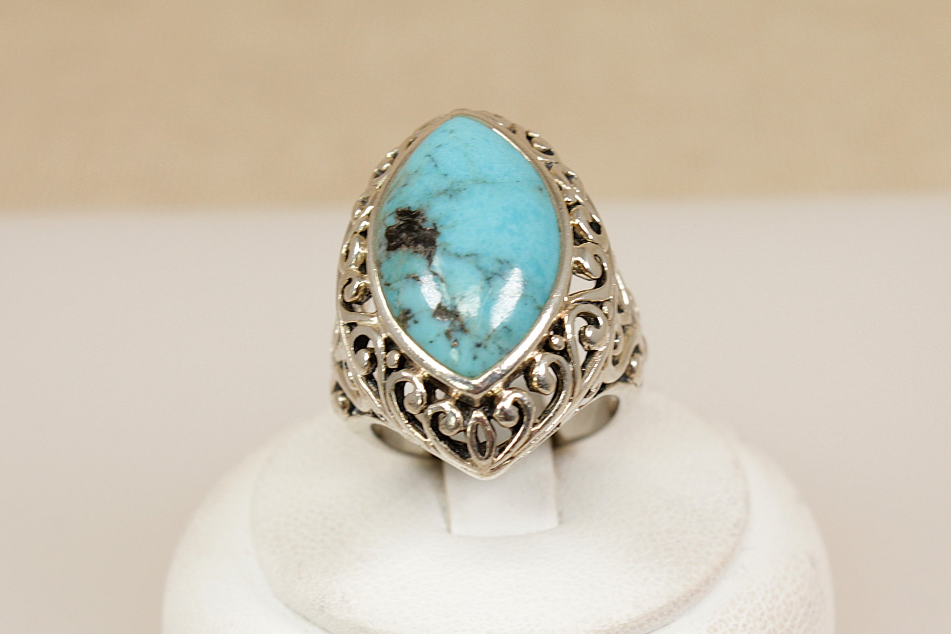Turquoise ring with silver band on a white stand against a beige background