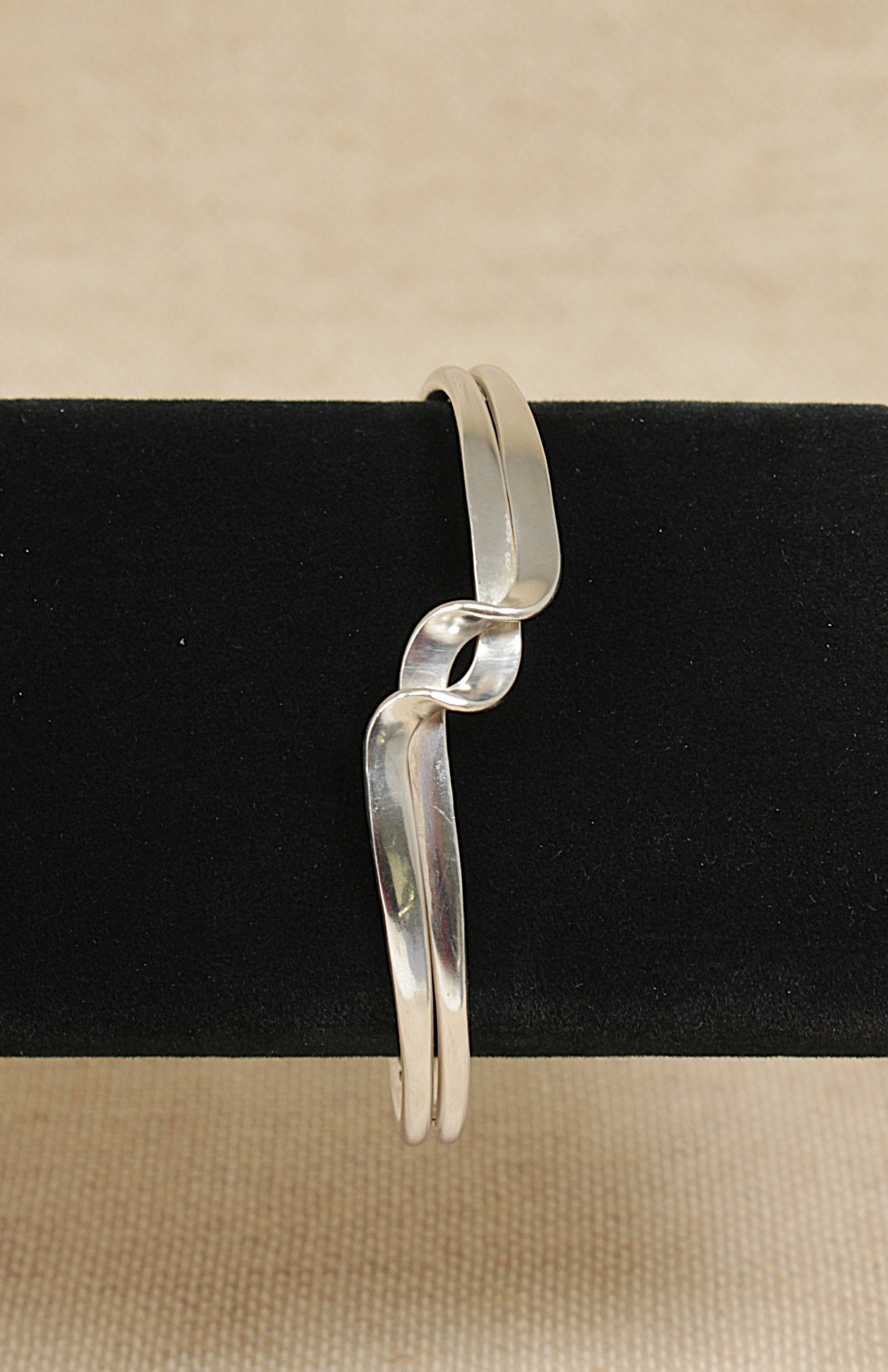 Silver bracelet on a black stand with a beige background