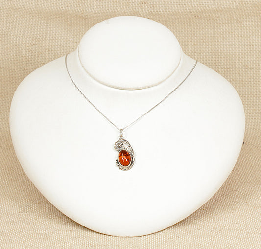 A beautifully crafted pendant featuring an oval piece of genuine Baltic amber, richly golden with delicate inclusions of ancient vegetation suspended within. The amber is bezel-set in finely detailed sterling silver, adorned with ornate floral motifs that echo the graceful curves of the Art Nouveau style. Expertly made and stamped 925 for sterling silver, this timeless piece hangs from an elegant 18-inch silver curb chain.