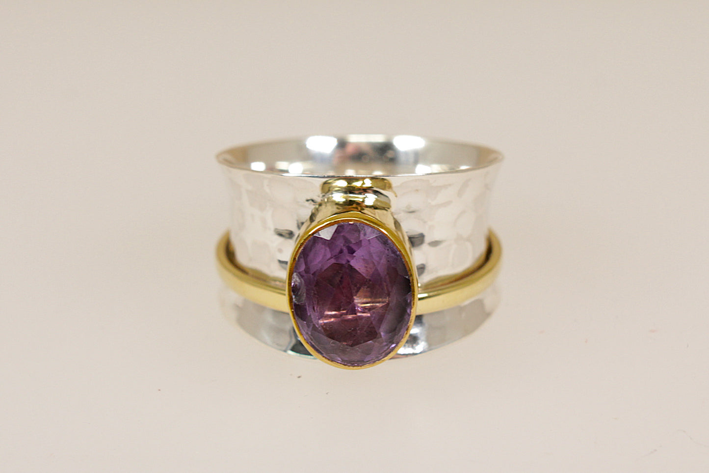 Two rings stacked on a beige background, one silver with a purple amethyst gemstone and the other silver gilt gold plated.
