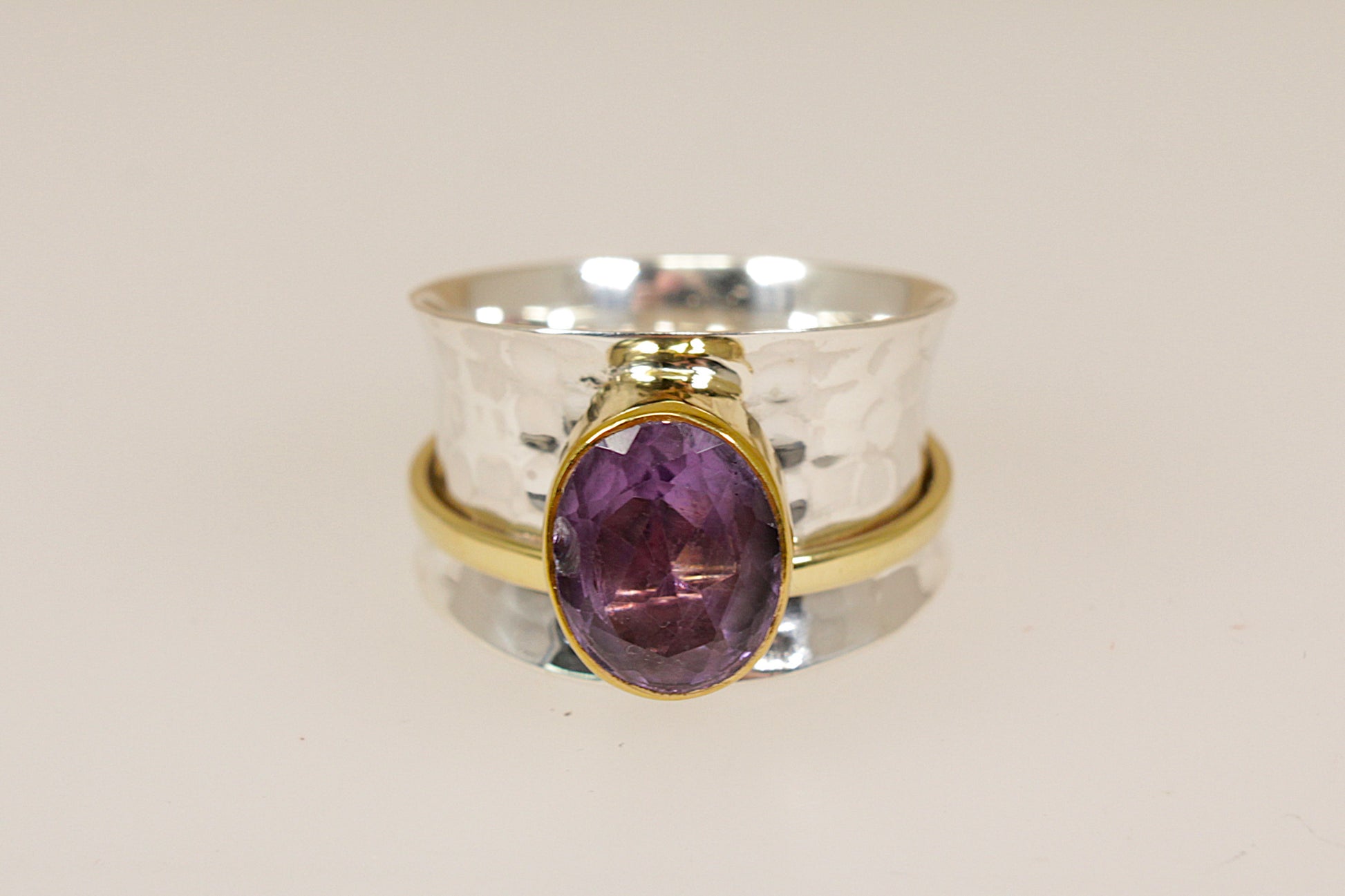Two rings stacked on a beige background, one silver with a purple amethyst gemstone and the other silver gilt gold plated.