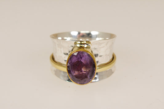 Two rings stacked on a beige background, one silver with a purple amethyst gemstone and the other silver gilt gold plated.
