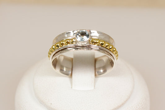 Silver ring with gold accents and a blue topaz gemstone on a white background