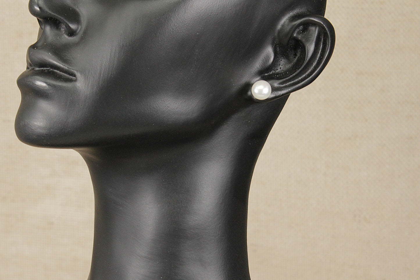 Mannequin head with a pearl earring on a beige background