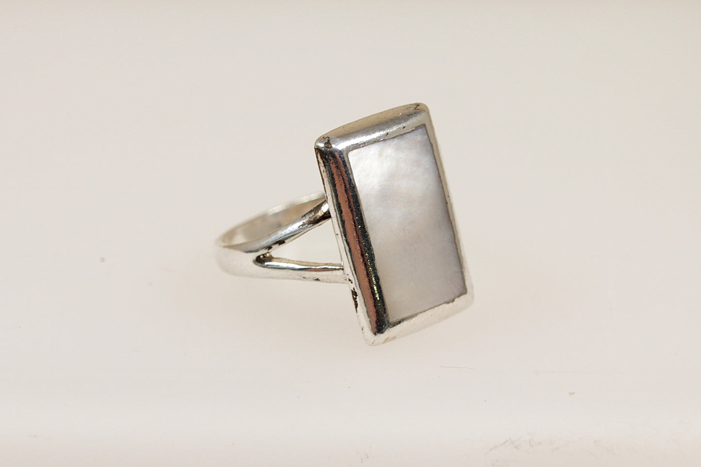 A silver ring with a rectangular mother of pearl inlay against a white background.